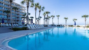 A hotel pool with sun loungers, palm trees, and a clear blue sky.