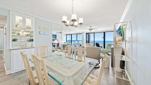 Ein großzügiger Essbereich mit Tischplatte aus Glas, Korbstühlen und Blick auf das Meer durch große Fenster.