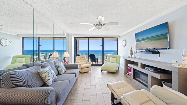Ein großzügiges Wohnzimmer mit großem Fernseher, bequemen Sitzgelegenheiten, einem Kamin und einem Balkon mit Meerblick.