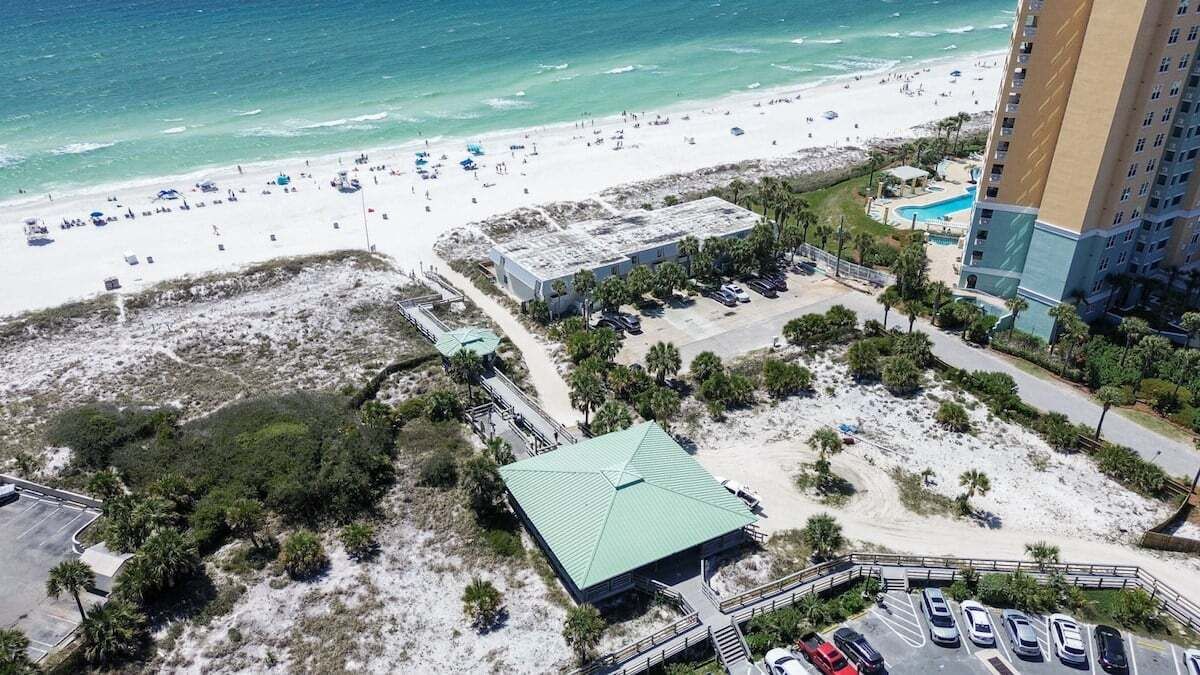 Vue aérienne d’un hôtel situé sur la côte, avec une plage, un parking et un espace piscine.