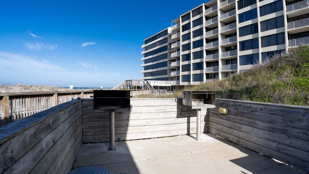 En träveranda med utsikt över en hög byggnad, ett trästaket och en klarblå himmel.