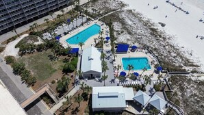 Vista aérea de un resort con dos piscinas, una playa y un estacionamiento.
