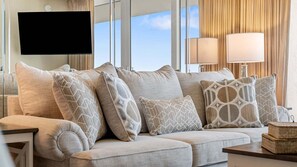 A modern living room with a sofa, patterned cushions, a flat-screen TV, and a lamp.
