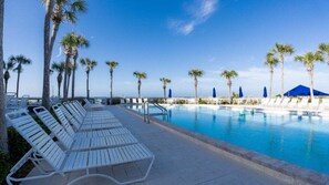 Zona junto a la piscina con sillones de descanso y palmeras.