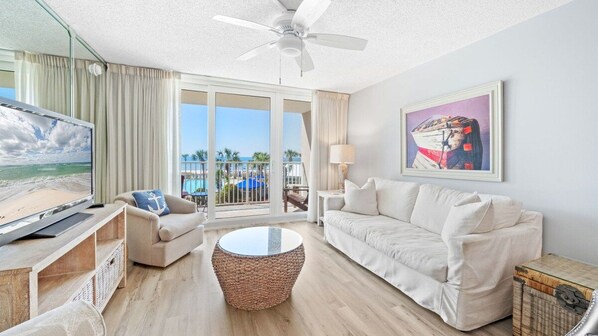 Habitación de hotel con balcón, televisión, sofá, mesa de centro y un cuadro.