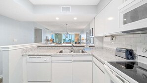 A modern kitchen with white cabinetry, a granite countertop, a built-in dishwasher, a stove, and a microwave. - Dunes B206-King Bed-Tennis/Pickleball-Pet Ok (Panama City Beach)