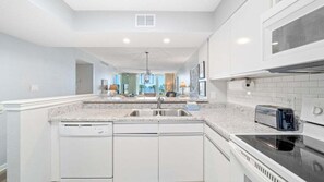 Une cuisine moderne avec des meubles blancs, un plan de travail en granit, un lave-vaisselle encastré, une cuisinière et un four à micro-ondes.