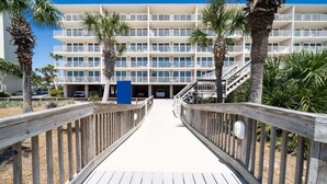 A multi-story hotel with a central walkway, palm trees, and a parking garage. - Dunes B206-King Bed-Tennis/Pickleball-Pet Ok (Panama City Beach)