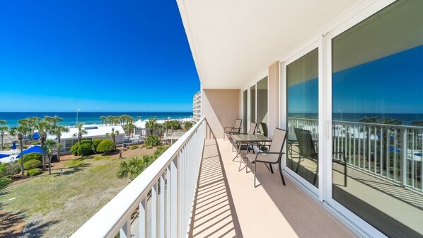 A balcony with a view of the beach and ocean, a table with chairs, and a railing.