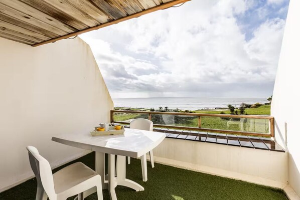 En balkon med bord og stole, en bakke med kopper og kande, samt udsigt over havet og landskabet.