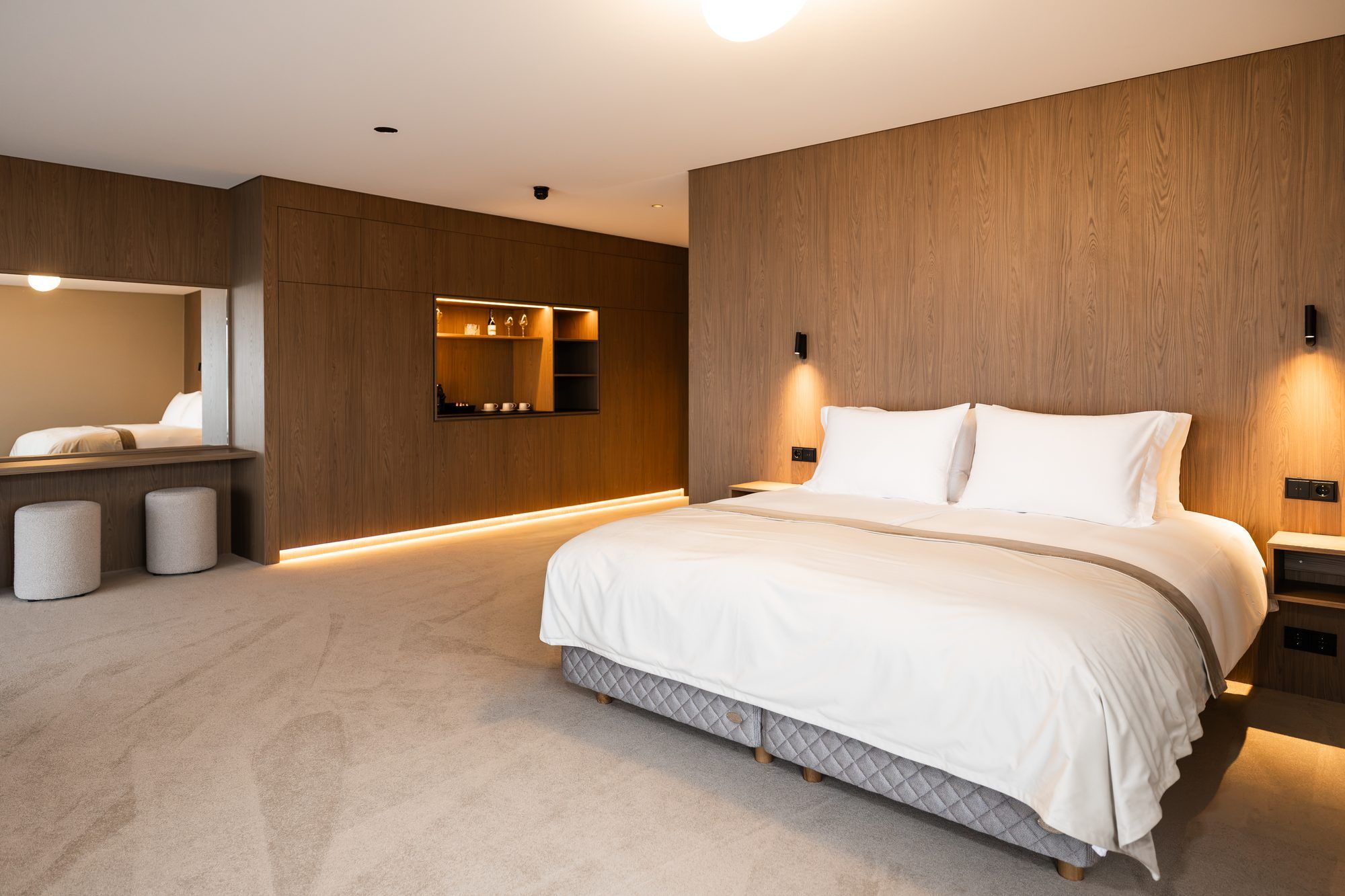 Un dormitorio moderno con una cama grande, mesitas de noche, un armario empotrado y un espejo.