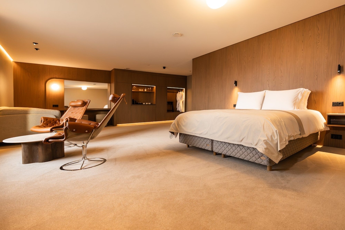 Een moderne hotelkamer met een bed, een zithoek met een stoel, een tafeltje en een spiegel.