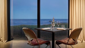A table set for two with a view of the ocean through large windows. - Black Sand Hotel (Sveitarfélagid Ölfus)