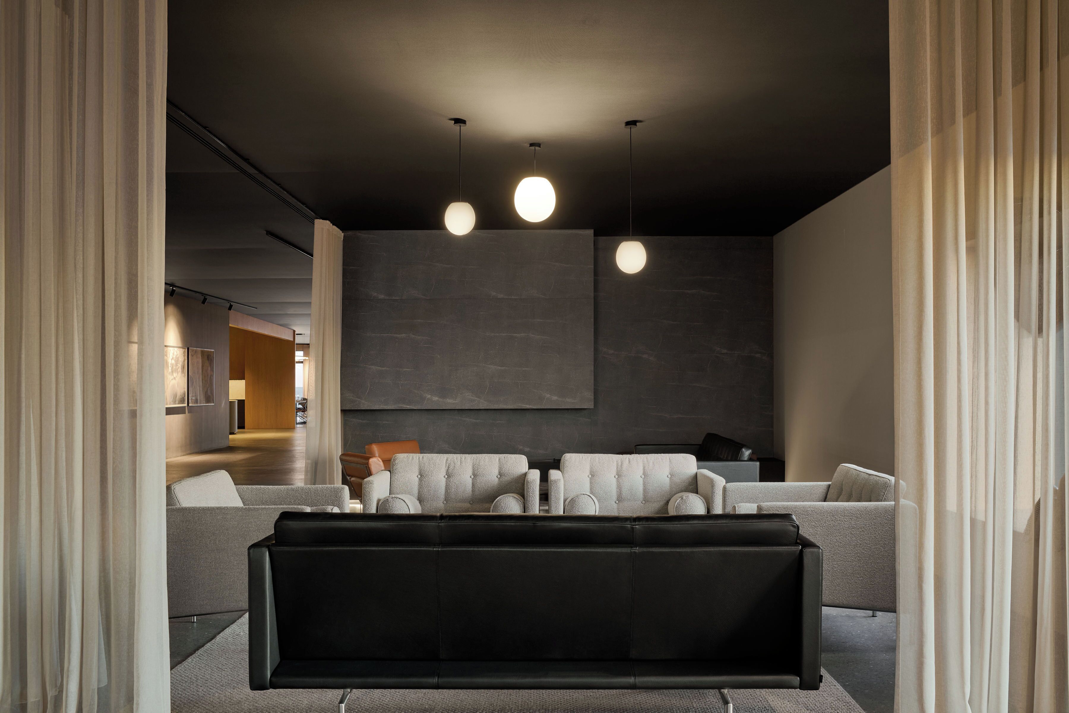 A modern living room with a sectional sofa, a black leather ottoman, and pendant lighting.
