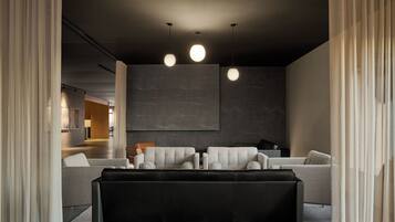 A modern living room with a sectional sofa, a black leather ottoman, and pendant lighting.