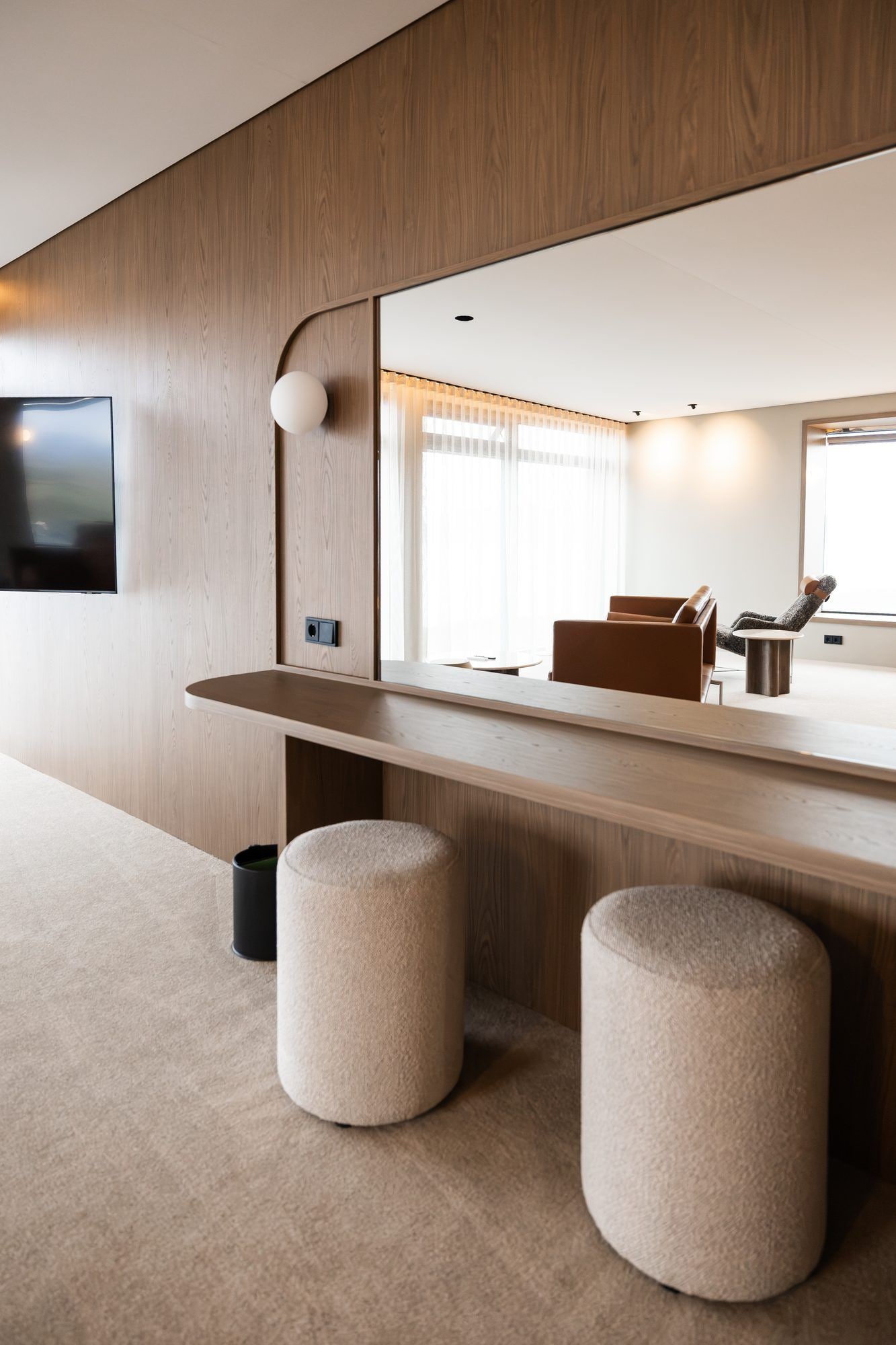Habitación de hotel moderna con una pared de acento de madera, un televisor de pantalla plana sobre un escritorio de madera y un espejo grande que refleja la habitación.