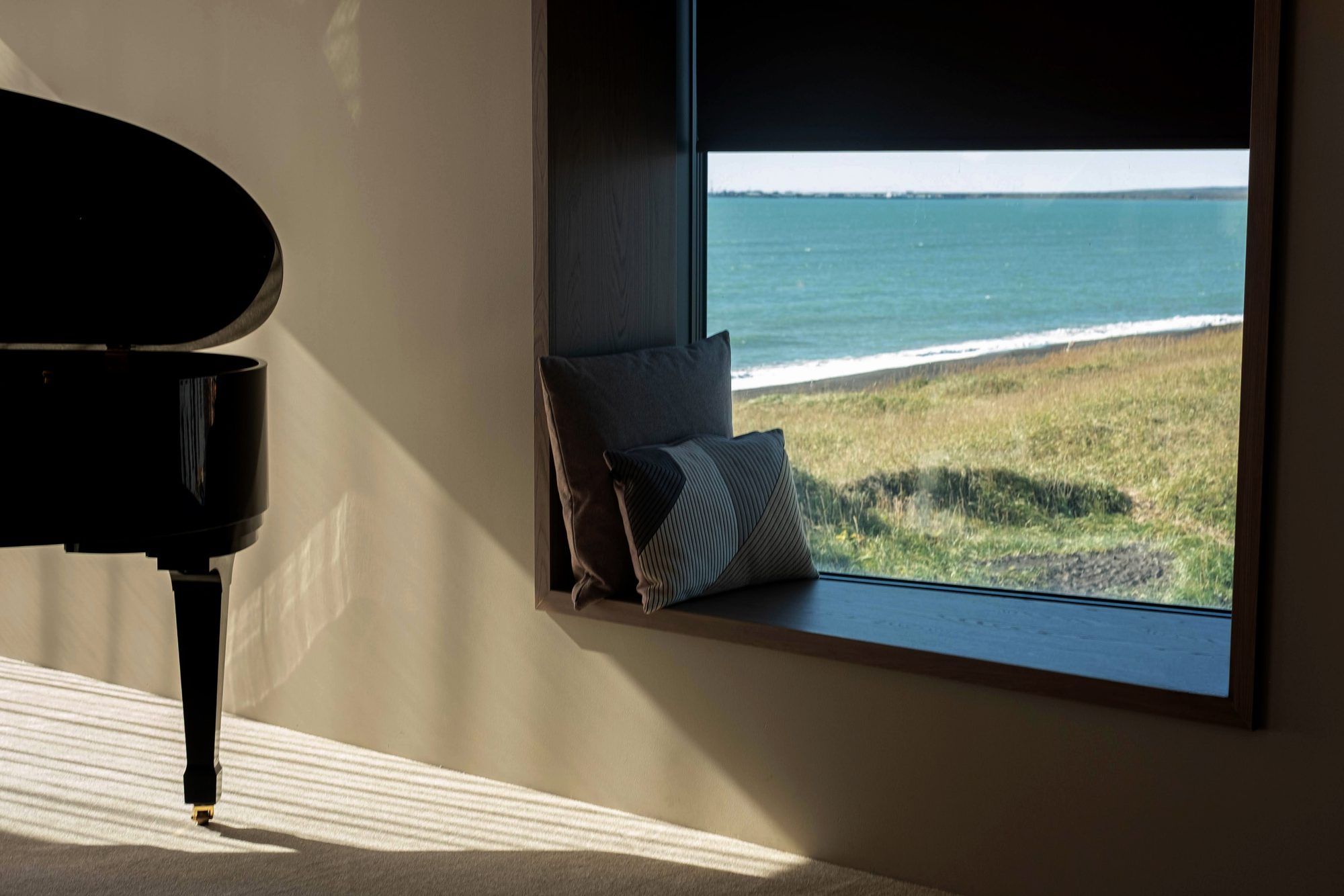 A piano in a room with a window overlooking a grassy area and the sea.