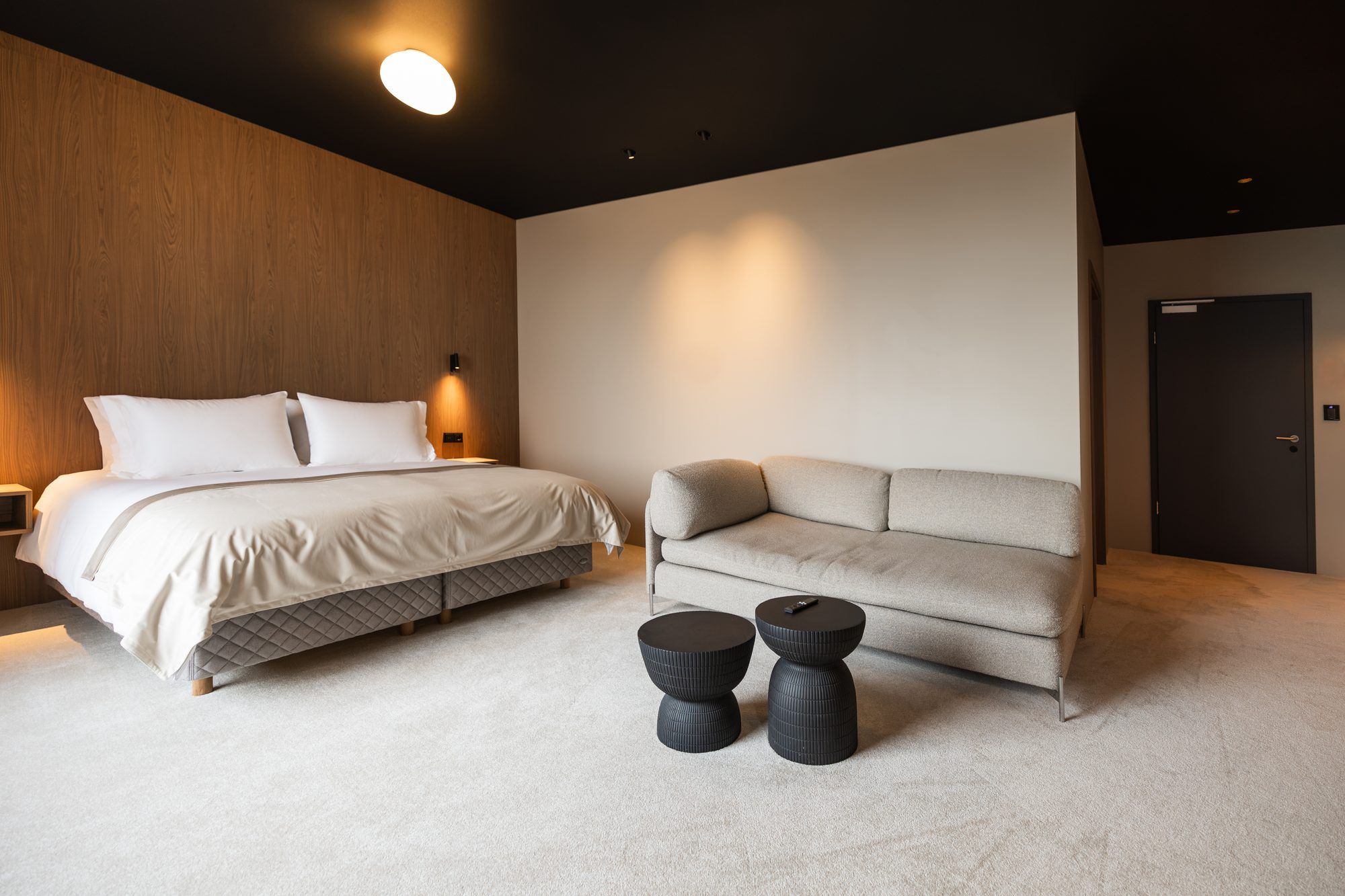 A modern bedroom with a bed, a sofa, two round side tables, and a door.