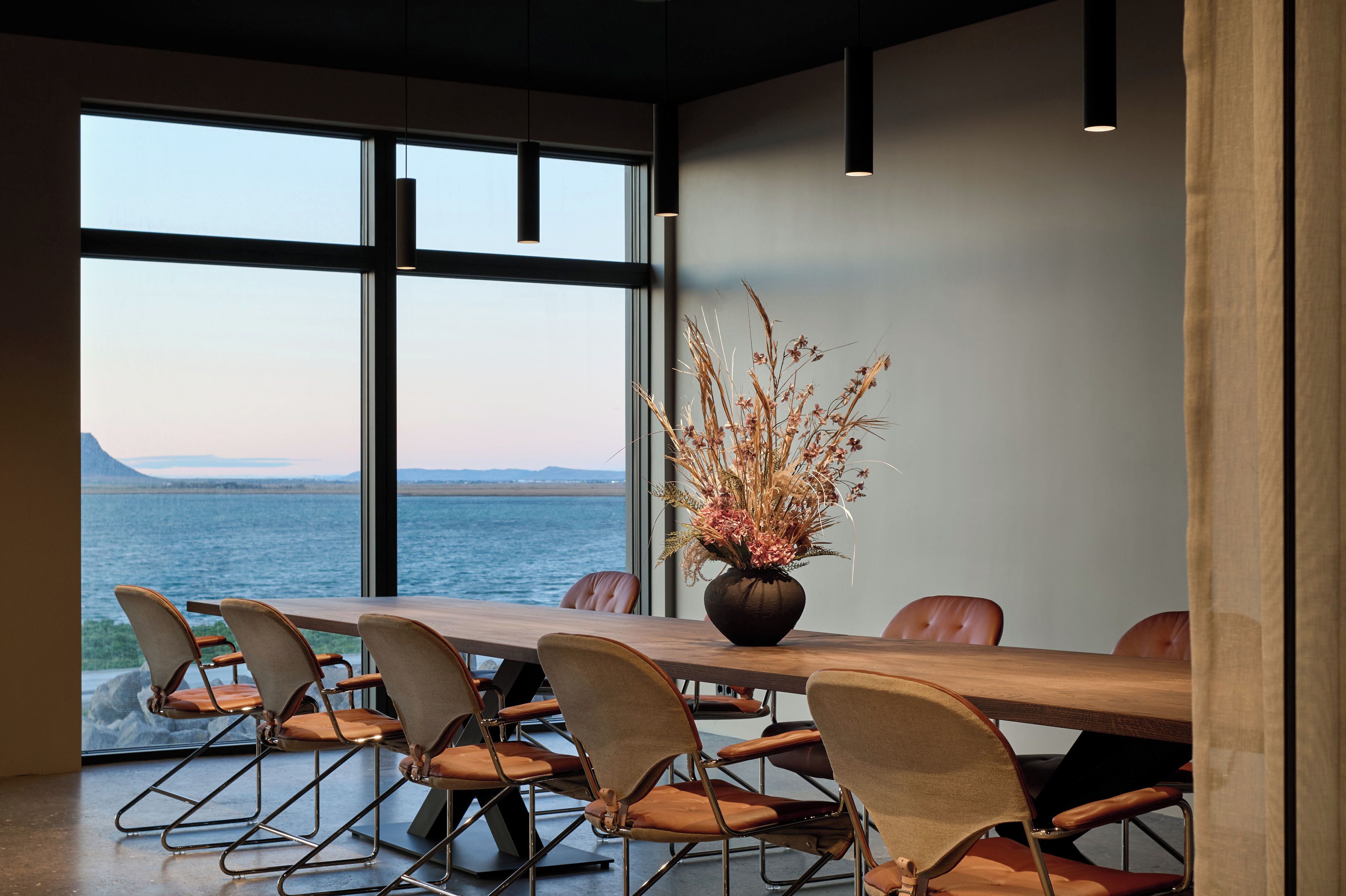 A conference room with a view of the sea, a wooden table, and modern chairs.
