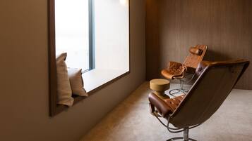 Una habitación con ventana, un sillón de cuero marrón, una mesa redonda y un espejo sujeto a la pared.