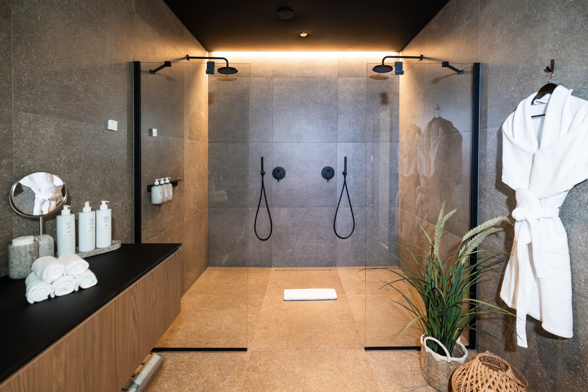 A modern bathroom with a glass shower enclosure, a wooden vanity, a mirror, and a white robe hanging on the wall.