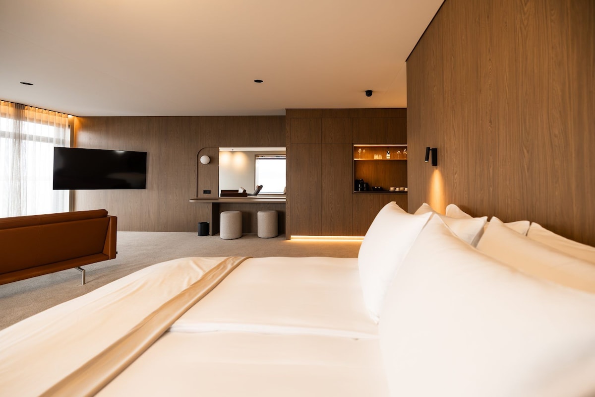 Een moderne hotelkamer met een groot bed, een flatscreen televisie, een houten accentmuur en een klein zithoekje.
