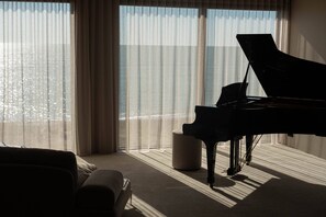Een vleugelpiano in een kamer met grote ramen, een bank en een klein voetenbankje.