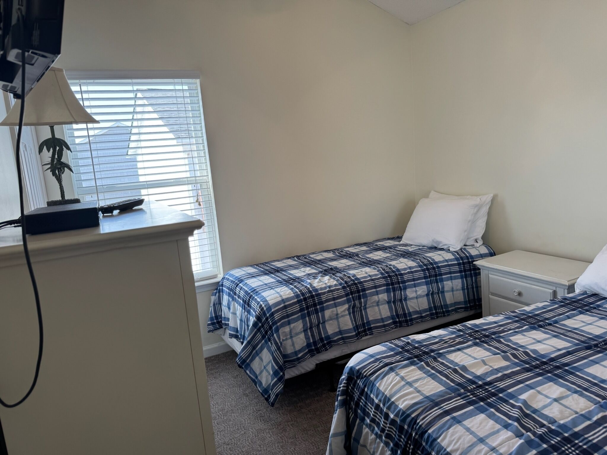 A bedroom with two beds, a nightstand, a lamp, and a window with blinds.
