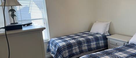 A bedroom with two beds, a nightstand, a lamp, and a window with blinds.