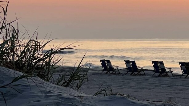 Una spiaggia con file di sedie a sdraio vuote che si affacciano sull'oceano, sotto un cielo al tramonto.