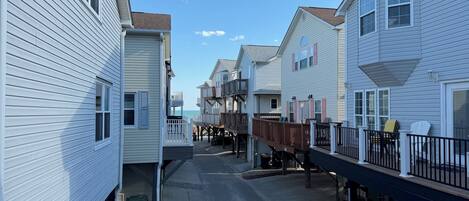 A narrow street with houses on either side, featuring balconies and a clear sky.