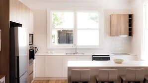 A modern kitchen with white cabinetry, a built-in island with seating, a stainless steel refrigerator, and a window providing natural light. - 'Sobrina' - A home away from home in Sandy Bay (Sandy Bay)
