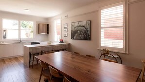 A modern kitchen with a central island, white cabinetry, and a dining area with a wooden table and chairs. - 'Sobrina' - A home away from home in Sandy Bay (Sandy Bay)