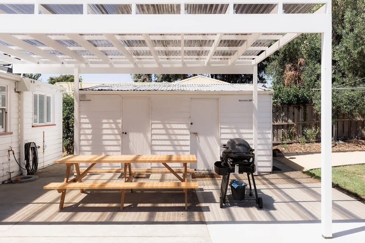 Ein überdachter Patio-Bereich mit einem Holztisch und einem Grill.