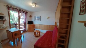Ett mysigt rum med ett skrivbord i trä, en röd soffa och en tv-apparat placerad på ett träskåp.