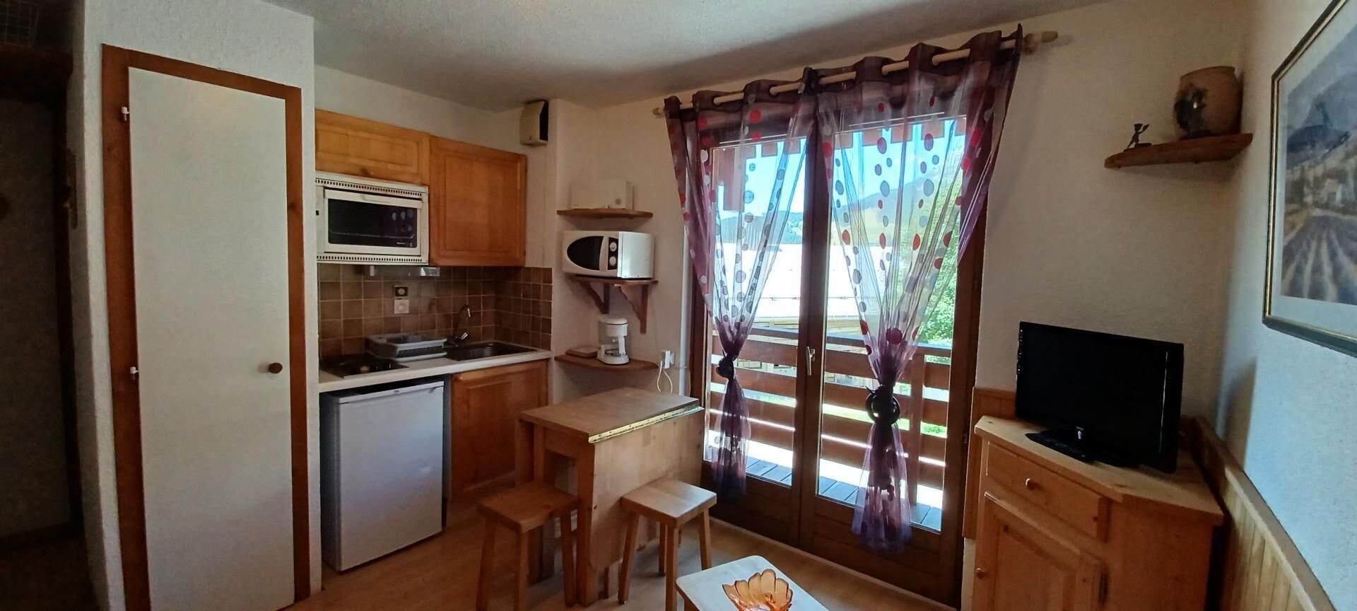 A compact kitchen with wooden cabinets, a built-in microwave, a refrigerator, and a small dining table.
