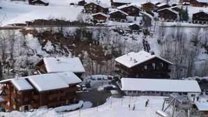 En snötäckt by med trähus, en skidlift och en bergskedja i bakgrunden.