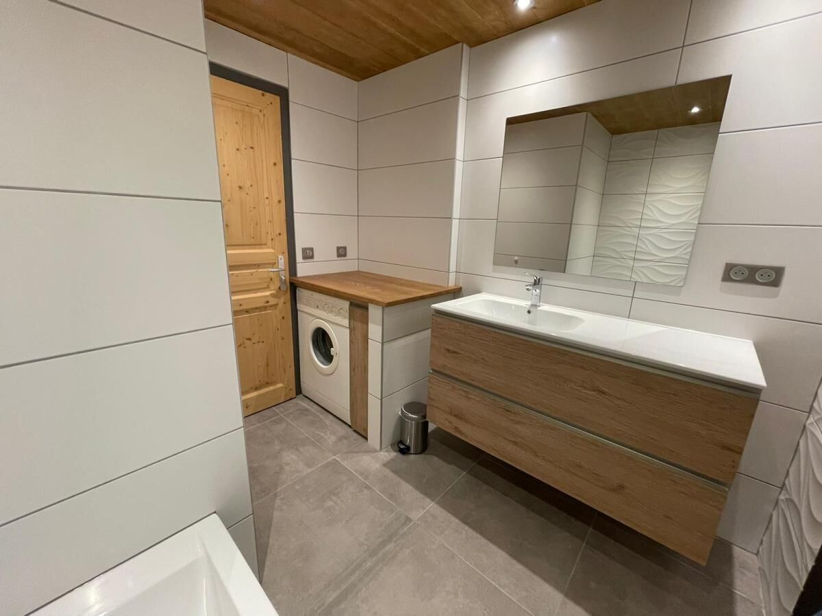 A modern bathroom with a wooden vanity, a built-in washing machine, and a large mirror.