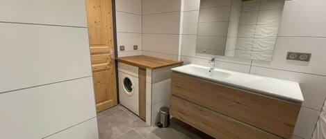A modern bathroom with a wooden vanity, a built-in washing machine, and a large mirror.