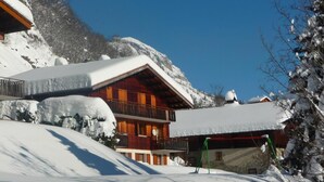 Eine mehrstöckige Holzchalet mit Balkon, umgeben von schneebedeckten Bergen.