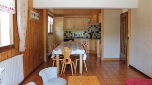 Ein Essbereich mit Tisch und Stühlen, eine Küche im Hintergrund, Holzwände und eine Heizung.