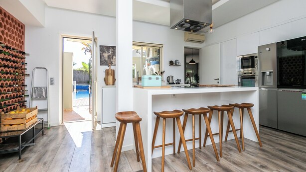 Uma cozinha moderna com uma ilha central, banquetas, eletrodomésticos de aço inoxidável e um espaço para vinhos.