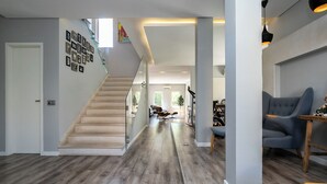Um interior moderno com escada de madeira, sala de estar com sofá azul e área de jantar com mesa e cadeiras.