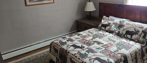 A bedroom with a bed, a nightstand, a lamp, a framed picture on the wall, and a window.