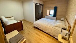 A wooden-paneled room with a bed, a chair, a small table, and a window with curtains.