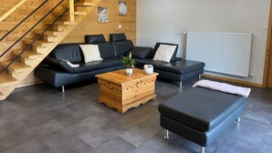 A modern living room with a wooden staircase, a black leather sofa, a wooden coffee table, and a black ottoman.