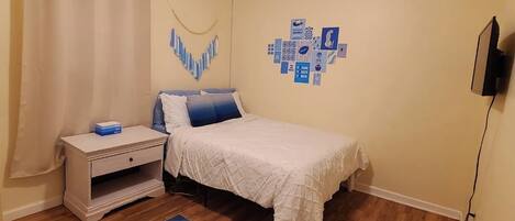Un dormitorio con cama, mesita de noche y televisor en la pared.