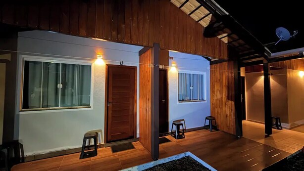 A modern house with a wooden exterior, large windows, and a covered porch area. - Pousada Suite Suzena (Penha)