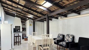 A dining area with a white table and chairs, a kitchen with a refrigerator, and a tiled floor. - Pousada Suite Suzena (Penha)