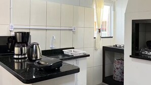 A compact kitchen with a black countertop, a stainless steel coffee maker, a kettle, and a small sink. - Pousada Suite Suzena (Penha)